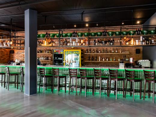 Long bar with a green glazed tile front, under-counter lighting and steel shelving against a brick wall