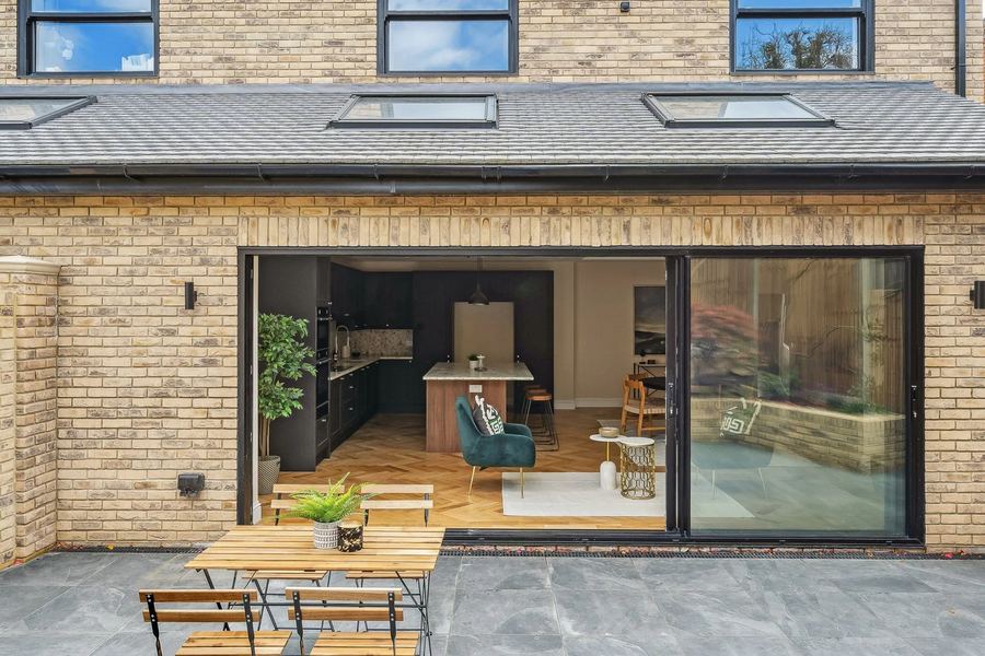 Yellow-brick rear extension with sliding doors open to a kitchen, seen from a slate patio