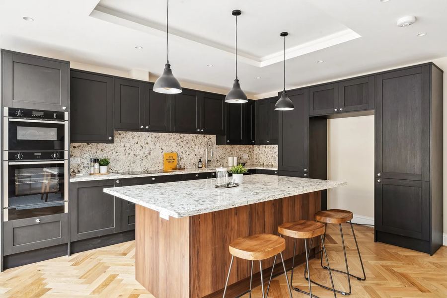 Dark shaker-style kitchen with a timber-clad island, stone worktops and pendant lights