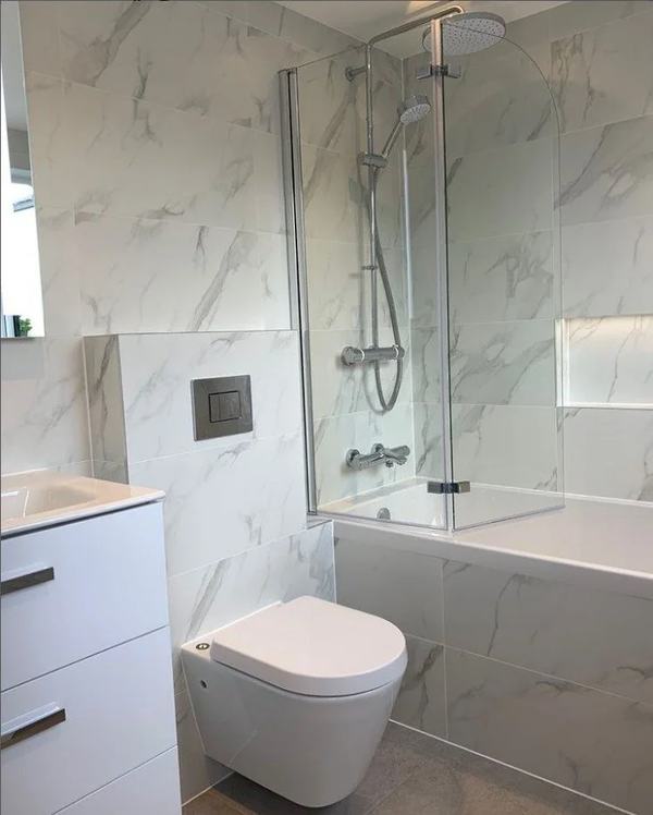 White bathroom with marble-effect tiles, wall-hung toilet and glass shower screen
