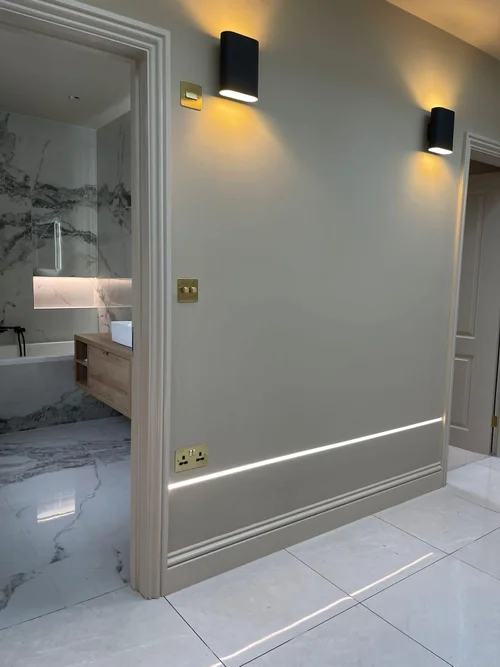 Hallway with wall lights and a recessed skirting light, looking into a bathroom
