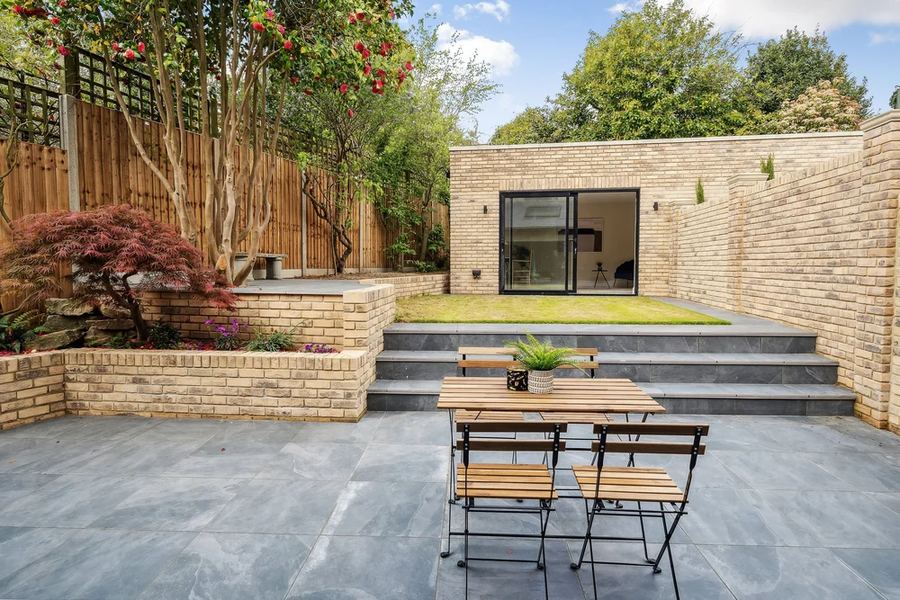 Brick garden building with glazed doors at the end of a terraced, paved garden