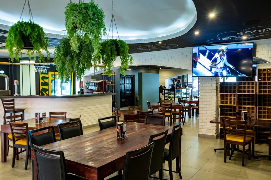 Restaurant dining room with timber tables, hanging planters, a curved feature ceiling and a white brick servery