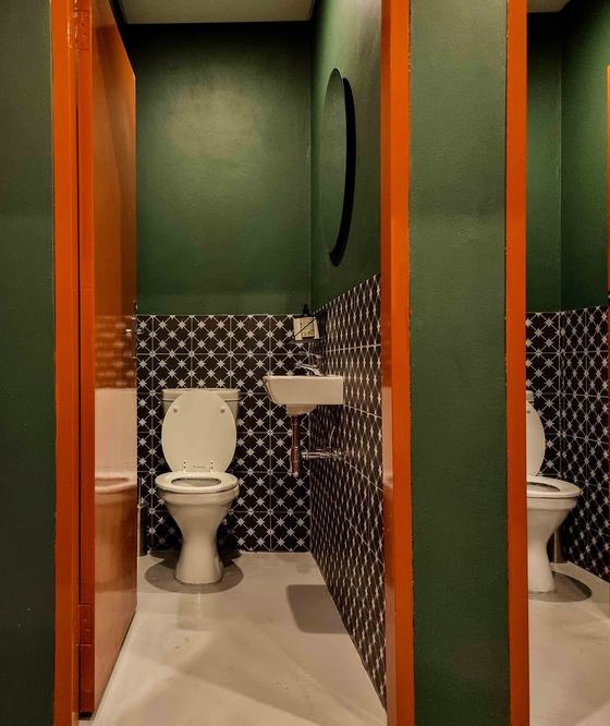 Washroom cubicles with patterned black and white wall tiles, green walls and orange doors
