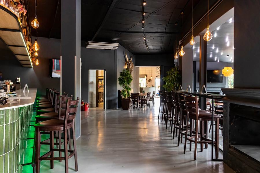 Dark-painted restaurant interior with bar stools, pendant lights and a polished concrete floor
